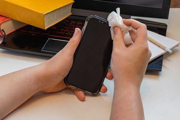 Eine Person reinigt den Bildschirm eines Smartphones mit einem weißen Tuch