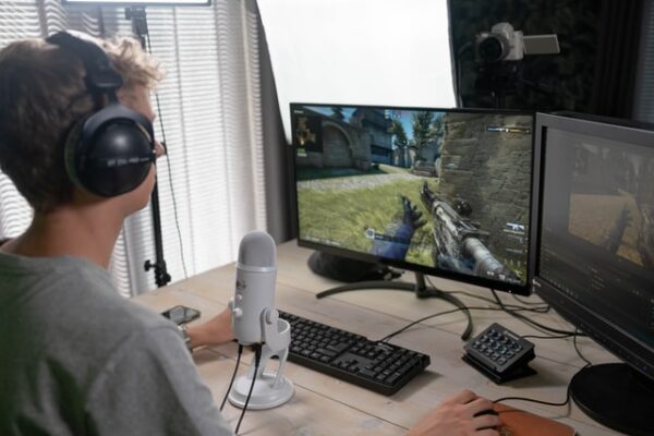 Ein Mann sitzt vor einem PC, ein Mikrofon vor ihm und ein Headset auf dem Kopf