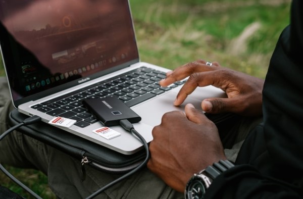 Eine Person arbeitet an einem Laptop, an dem eine Festplatte angeschlossen ist und auf dem zwei SD-Karten liegen.