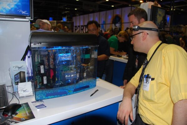 Eine Gruppe Männer schaut auf einen ölgelühlten Computer, der wie ein Aquarium gestaltet ist. 