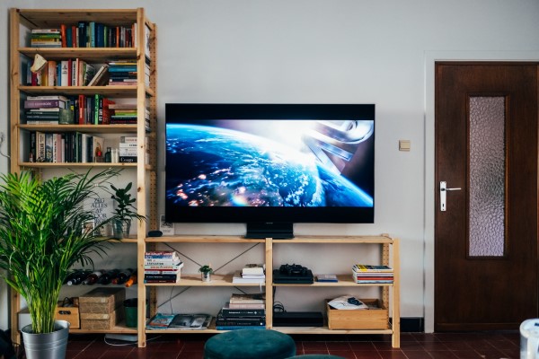 Ein flacher Fernseher auf einem Holzregal vor einer hellen Wand.