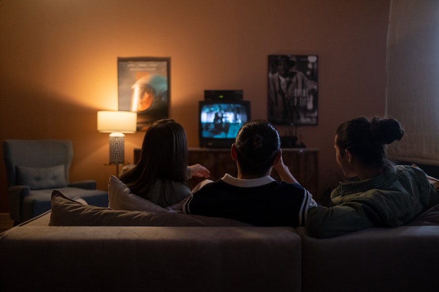 Drei Personen sitzen auf einer Couch und schauen zusammen auf einen kleinen Fernseher.