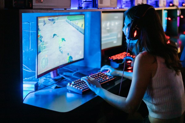 Eine Frau mit Kopfhörern sitzt vor einem Curved-Monitor und spielt ein PC-Game.