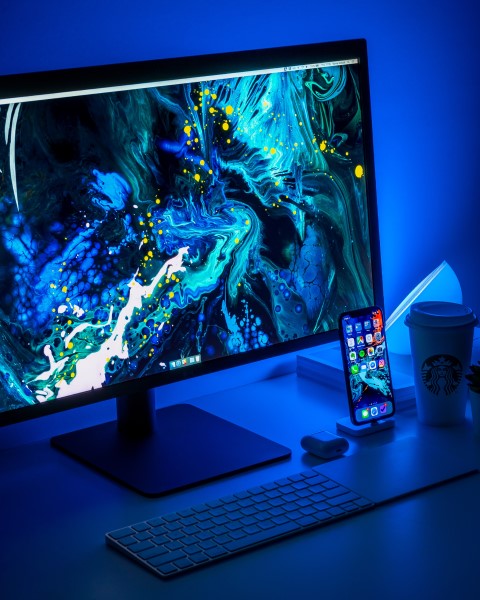 Ein Monitor mit abstraktem Bild steht neben einem Handy auf einem Schreibtisch mit blauem Hintergrund.