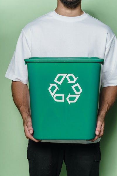 Ein Mann hält einen grünen Müllkorb mit dem Recycling-Symbol.