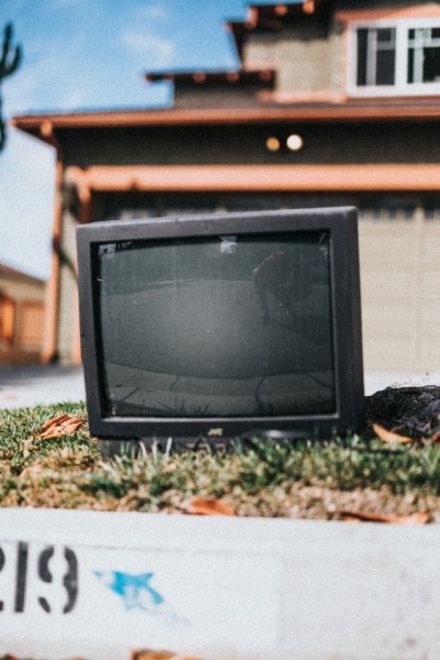 Ein alter Röhrenfernseher steht auf dem Rasen vor einem Haus. 