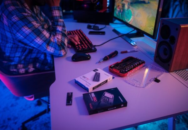 Eine Person spielt an einem Gaming PC. Auf dem Tisch liegen zwei SSDs.
