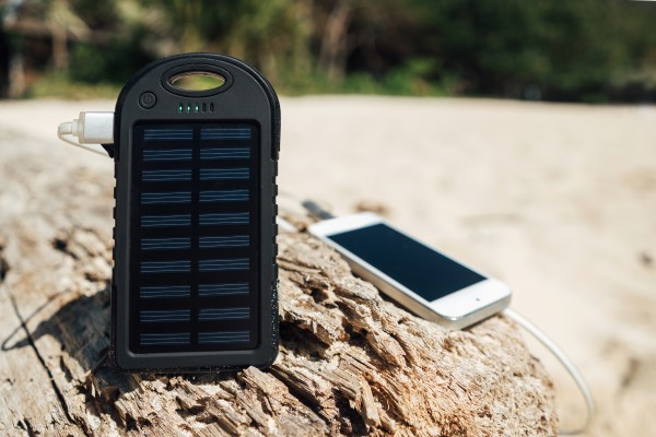 Eine Solar-Batterie lädt ein Smartphone auf einem Stein am Strand. 