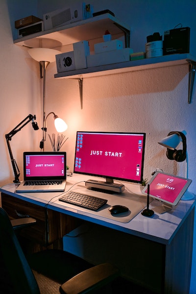 Ein Schreibtisch mit drei Bildschirmen auf denen allen Just Start steht.