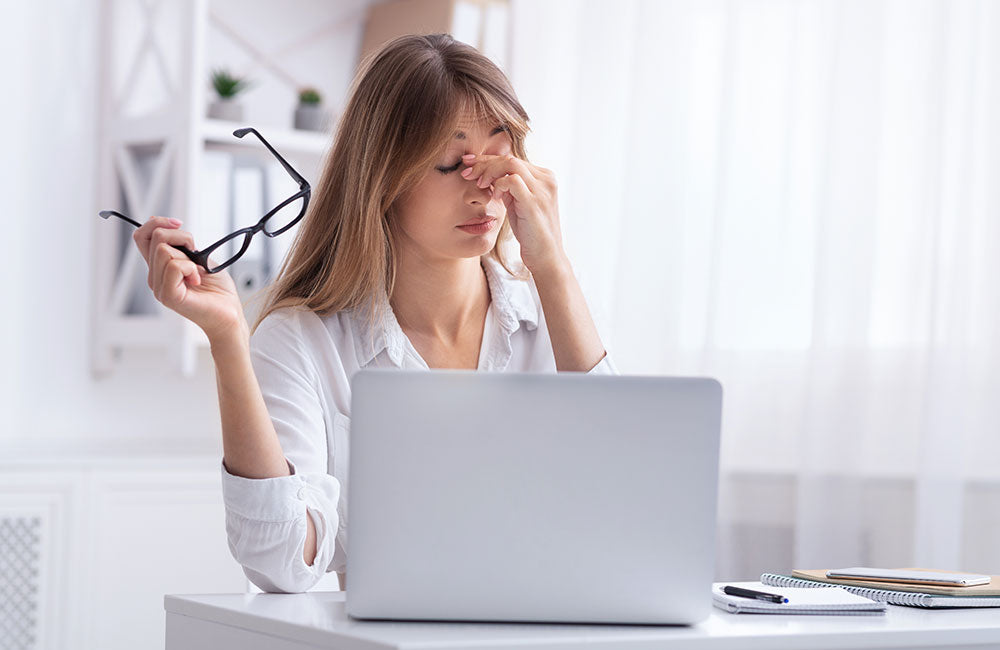 Überarbeitete Frau massiert Nasenrücken Sitzen am Laptop am Arbeitsplatz