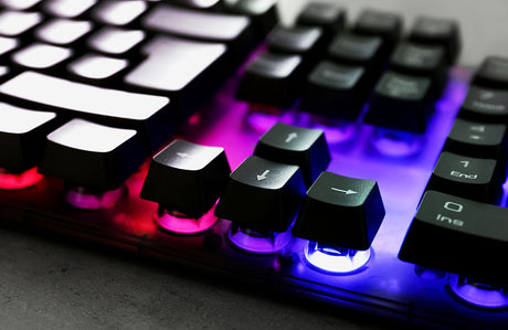 Nahaufnahme einer Gaming-Tastatur mit RGB-Beleuchtung auf einer grauen Tischplatte